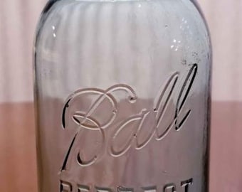 Peut inclure: Un bocal Ball Perfect Mason teinté de bleu vintage avec un couvercle en métal. Le bocal présente des lettres en relief qui se lisent "Ball PERFECT MASON". Le bocal est en verre et est probablement utilisé pour la mise en conserve ou le stockage.