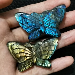 Op de afbeelding: Twee gesneden vlindersculpturen van labradoriet. De vlinder links is blauw en iriserend, terwijl de vlinder rechts groen en goud is.