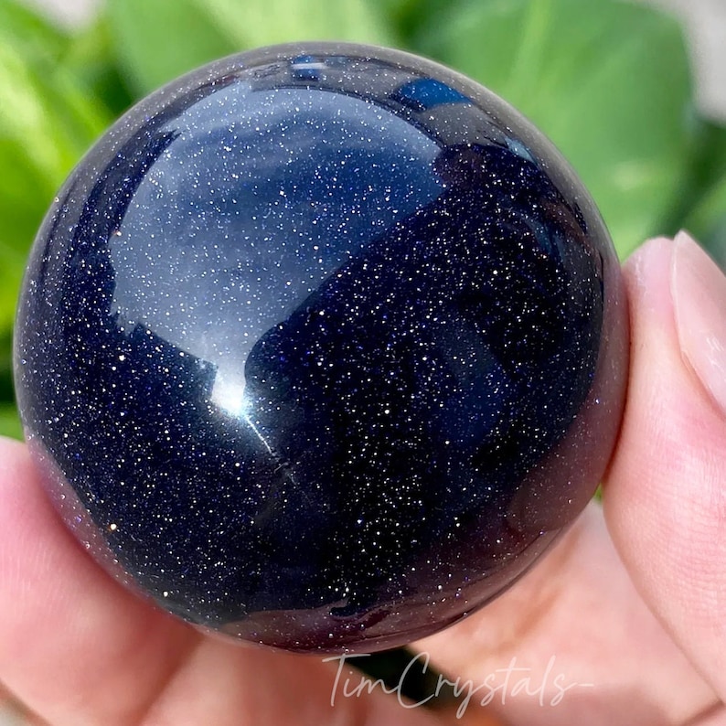 May include: A polished dark blue sphere with a sparkly, starry appearance. The sphere is made of blue sandstone.