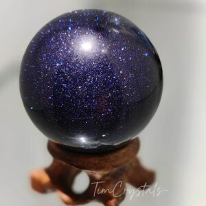 May include: A dark blue sphere with a glittery finish, resembling a starry night sky. The sphere is displayed on a wooden stand.