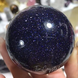May include: A polished blue sphere with a sparkly, starry appearance. The sphere is made of blue sandstone and has a smooth, shiny surface.