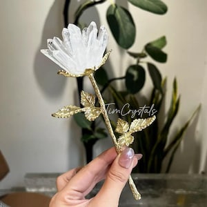 May include: A decorative crystal rose with a clear, faceted crystal flower head and a gold-colored stem and leaves. The stem is textured, and the leaves have intricate detailing. The rose is a unique home decor item.