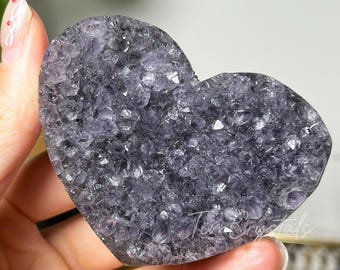 May include: A heart-shaped amethyst crystal with a cluster of small, purple crystals. The crystal is smooth and polished, with a natural, raw edge.