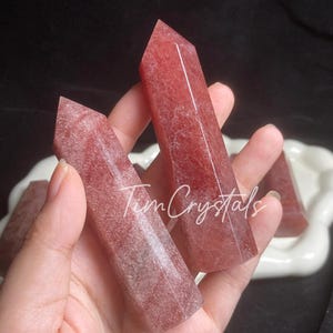 以下が含まれることがあります： 手の中に、ローズクォーツとしても知られるピンクと白のクリスタルポイントが3つあります。ポイントは滑らかで、自然で素朴な外観をしています。
