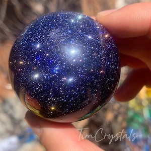 May include: A dark blue sphere with a glittery surface, resembling a night sky with stars. The sphere is made of polished stone and has a smooth, reflective finish.