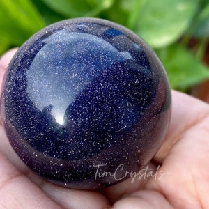 May include: A dark blue sphere with a glittery, starry appearance. The sphere is made of polished stone and has a smooth, reflective surface.