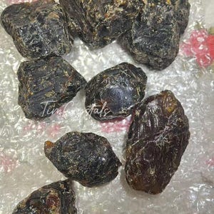 May include: A selection of raw, dark brown amber stones. The amber pieces are of various sizes and shapes, with a glossy, textured surface. The text "Tim Crystals" is visible on the surface.