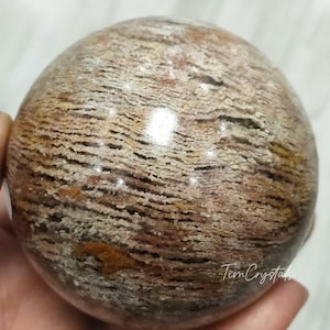 May include: A large, round, brown and white agate sphere with a layered, striated pattern. The sphere is polished and has a glossy finish.