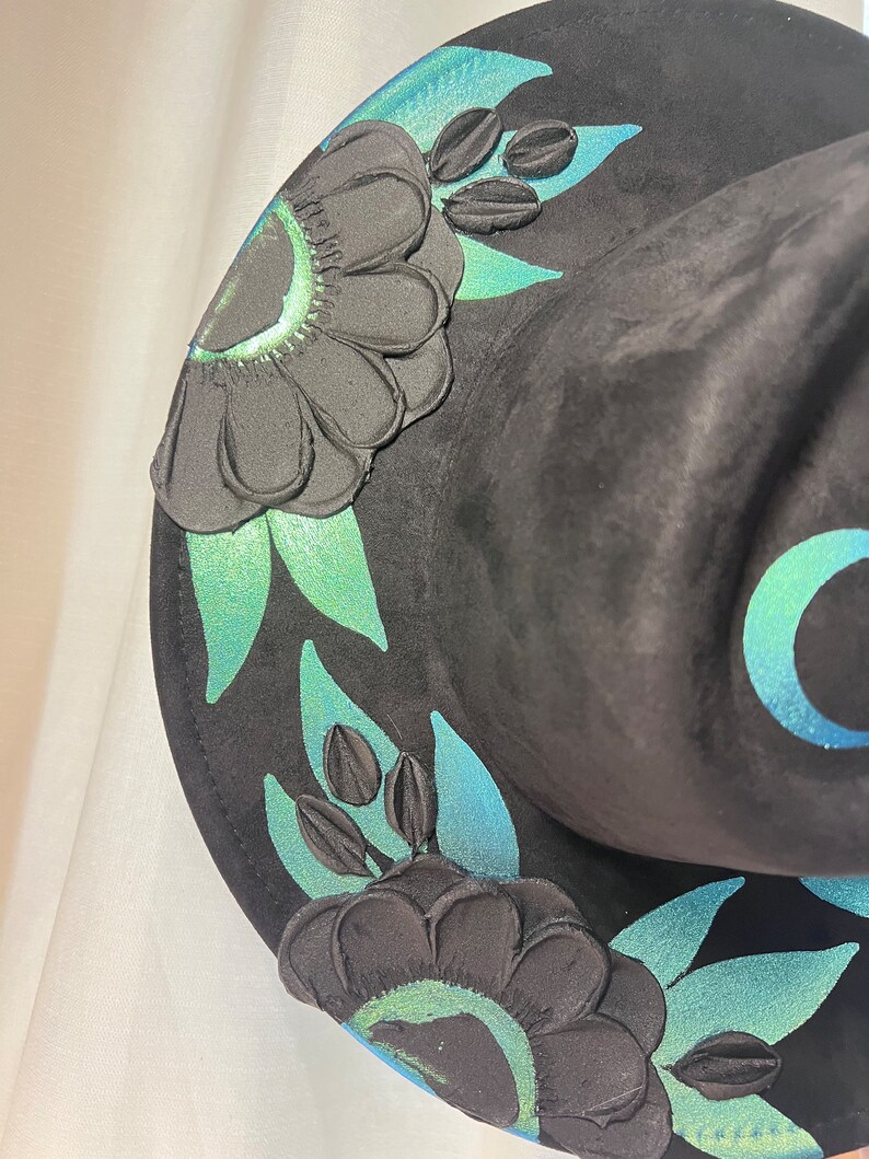 May include: Black witch hat with green and blue floral embroidery. The hat has a wide brim and a tall crown.