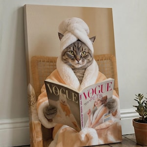 Puede incluir: Un lienzo impreso que muestra a un gato atigrado con una toalla blanca envuelta en la cabeza y un albornoz de felpa color melocot&oacute;n. El gato est&aacute; sentado en una silla de mimbre y sostiene una revista abierta titulada Vogue Pets.