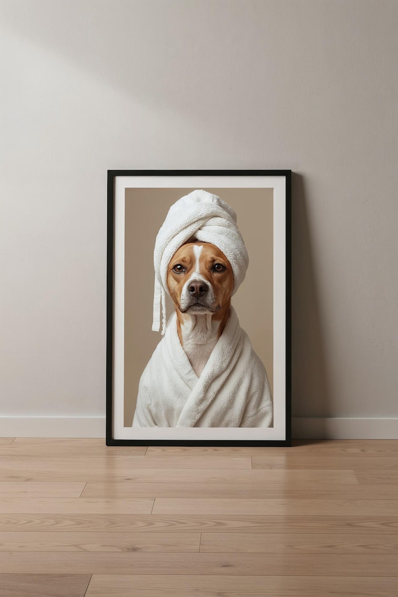 Puede incluir: Una impresi&oacute;n art&iacute;stica enmarcada que muestra a un perro de color canela y blanco con un albornoz de felpa blanco y una toalla blanca a juego envuelta alrededor de la cabeza. El retrato tiene un fondo beige neutro y un marco negro.
