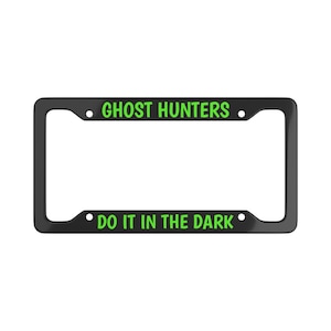 Könnte beinhalten: Schwarzer Kennzeichenrahmen mit dem Text "GHOST HUNTERS" oben und "DO IT IN THE DARK" unten, beide in Grün. Der Rahmen hat eine rechteckige Form mit abgerundeten Ecken.