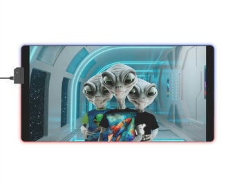 May include: Three gray alien figures with large eyes and mouths stand in a futuristic hallway. The alien in the middle is wearing a blue, green, and orange shirt with a rocket ship design. The alien on the left is wearing a green shirt with an alien design. The alien on the right is wearing a black shirt. The hallway is lit with blue neon lights.