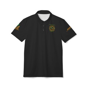 May include: Black polo shirt with a white collar and three buttons. The shirt features green and gold text and a logo on the sleeves and chest. The text on the sleeves reads "Station 51" and "STATIC". The chest logo includes the words "FIRE DEPARTMENT" and "MADERA, CA".