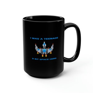 Könnte beinhalten: Schwarze Kaffeetasse mit einem weißen Design, auf dem "Ich war ein 8-Bit-Weltraumheld im Teenageralter" steht, mit einer pixelartigen Raumschiffgrafik.