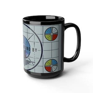 May include: Black ceramic mug with a vintage television test pattern design. The pattern includes a circle with the words "STAND BY" and a color wheel with numbers.