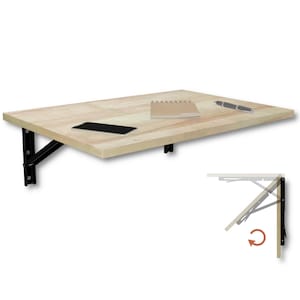 Può includere: Una scrivania pieghevole a parete in legno chiaro con supporti in metallo nero. Sulla superficie si trovano uno smartphone nero, un taccuino a spirale e una penna. Un piccolo diagramma nell'angolo mostra il meccanismo di chiusura.