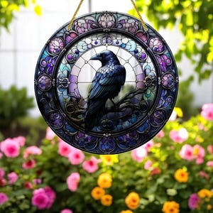 Puede incluir: Adorno de pared redondo que representa un cuervo posado en una rama, con un diseño de vidriera. La obra de arte utiliza tonos de azul, morado y verde, con una cuerda dorada para colgar. El fondo muestra un jardín con flores rosas y amarillas.