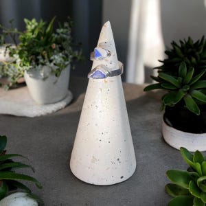May include: A silver ring with two blue and white triangular pieces of glass set on a white cone-shaped ring holder.