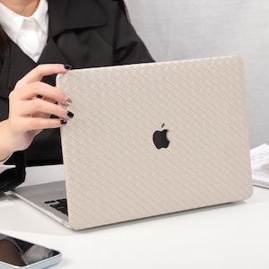 Puede incluir: Una funda para portátil beige con textura tejida y el logotipo de Apple. La funda está cerrada y el portátil no es visible.