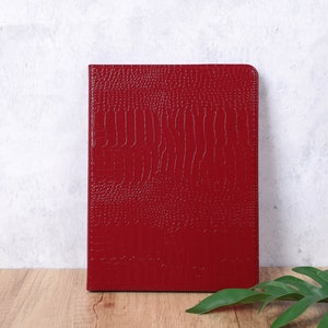 May include: A red leather notebook with a crocodile embossed pattern.
