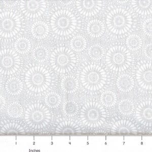 May include: A light gray fabric featuring a repeating pattern of white circular floral motifs. A ruler is visible at the bottom edge, showing a scale in inches from 1 to 8, indicating the size of the repeating circular design elements.