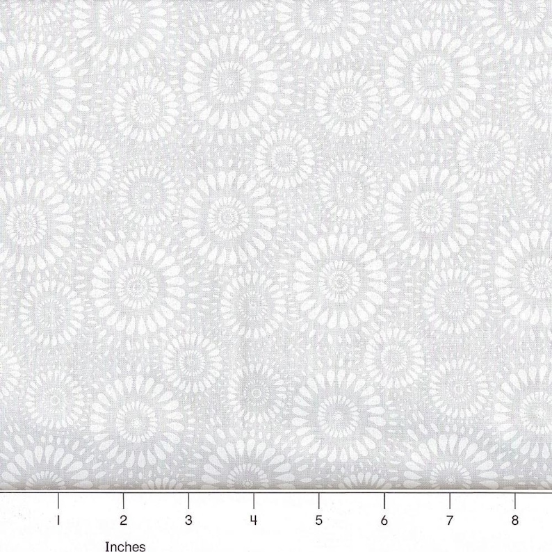 May include: A light gray fabric featuring a repeating pattern of white circular floral motifs. A ruler is visible at the bottom edge, showing a scale in inches from 1 to 8, indicating the size of the repeating circular design elements.