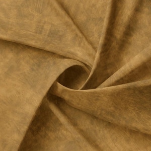 May include: A close-up of a brown fabric with a textured, slightly mottled appearance. The fabric is folded and draped, creating a soft, flowing look.