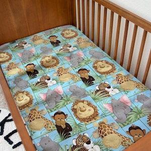 May include: A blue and green crib sheet with a repeating pattern of jungle animals, including a giraffe, lion, monkey, tiger, and elephant. The animals are all smiling and have friendly faces.