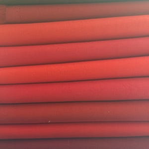 May include: A collection of folded fabric pieces in a spectrum of reds, from dark burgundy to vibrant scarlet. The material seems to be closely woven, with a discernible texture. The folds create a layered effect, highlighting the colour variations.
