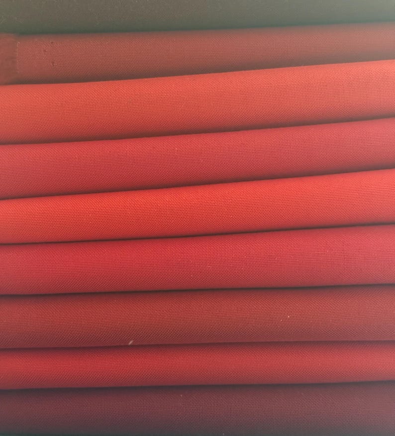 May include: A collection of folded fabric pieces in a spectrum of reds, from dark burgundy to vibrant scarlet. The material seems to be closely woven, with a discernible texture. The folds create a layered effect, highlighting the colour variations.