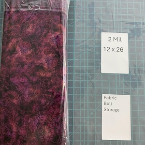 以下が含まれることがあります： 透明なプラスチックで包まれた生地のロール。生地は濃いバーガンディ色の花柄です。「2 Mil 12 x 26」と書かれたカードと「Fabric Bolt Storage」と書かれたカードが2枚見えます。
