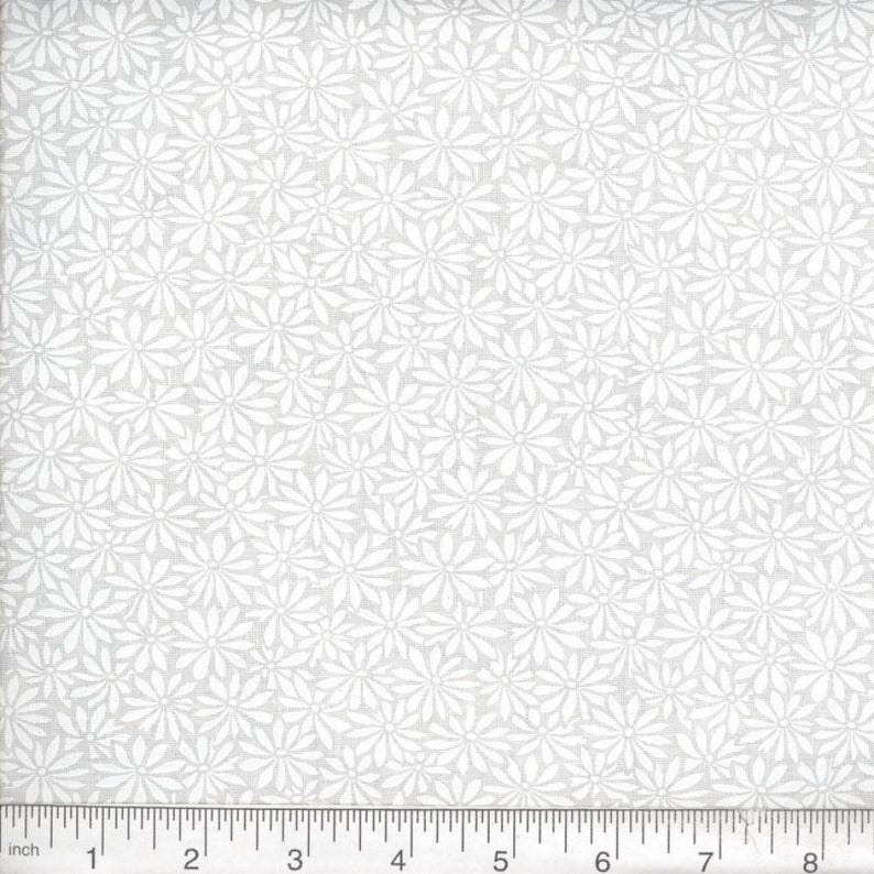 May include: A light gray fabric featuring a repeating pattern of white daisy-like flowers. A ruler is positioned along the bottom edge, showing a scale of 8 inches, providing a clear visual reference for the size of the floral print design.