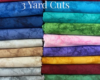 Op de afbeelding: Een stapel gevouwen stoffen in diverse kleuren zoals rood, blauw, groen, roze, paars, geel, bruin, grijs en zwart, allemaal met een gemarmerde textuur. De tekst 3 Yard Cuts staat in het wit bovenaan de afbeelding gedrukt.