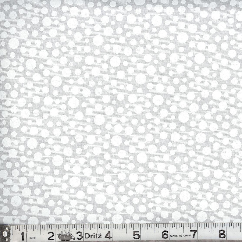 May include: A light gray fabric featuring a pattern of white polka dots of varying sizes. A Dritz measuring tape is positioned along the bottom edge, showing a length of 8 inches with clear black markings on a white background for scale.