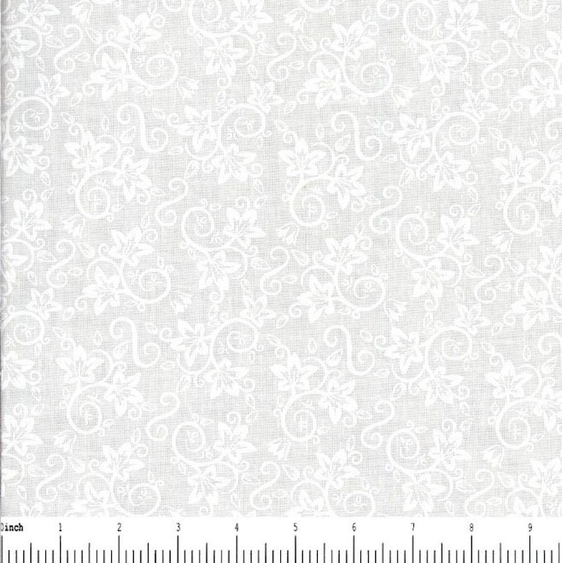 May include: A white fabric featuring a repeating pattern of light gray floral vines and leaves. A ruler is visible at the bottom edge, showing a scale in inches, with the fabric pattern extending across the full width of the frame.
