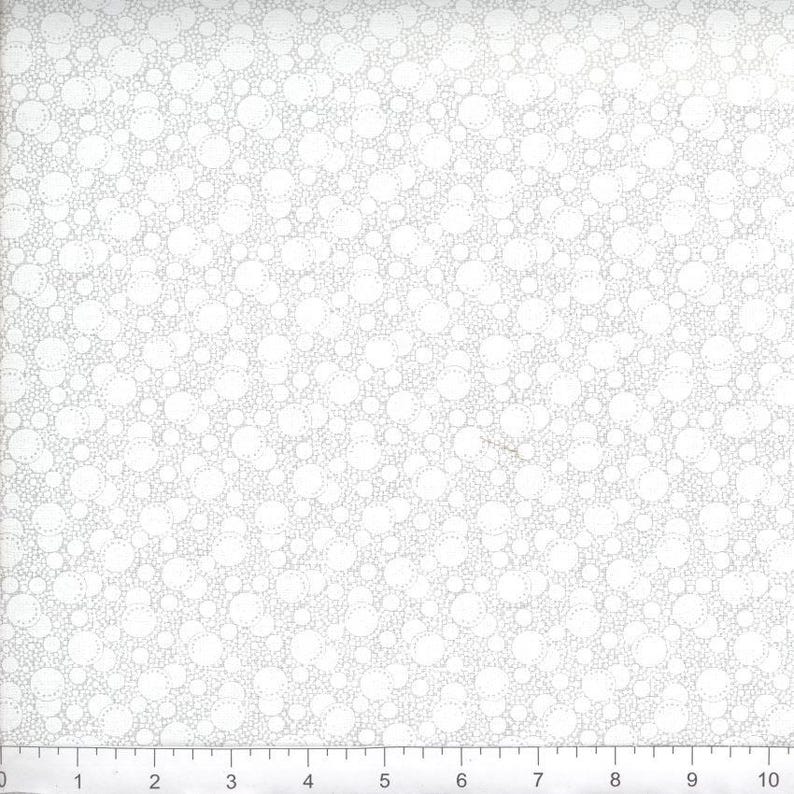 May include: A white fabric featuring a repeating pattern of light gray circles of varying sizes. A ruler is visible at the bottom edge, showing a scale of 10 inches, with each numbered increment representing one inch of the fabric's width.