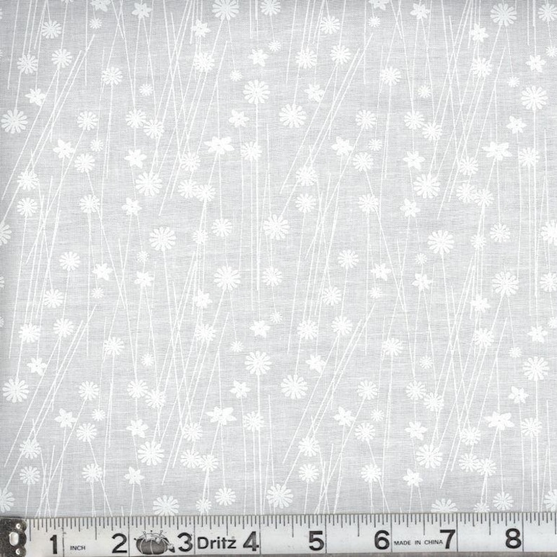 May include: A light gray fabric featuring a repeating pattern of white line-drawn flowers and thin vertical stems. A Dritz brand measuring tape is positioned at the bottom, showing a scale of 8 inches across the width of the textile material.