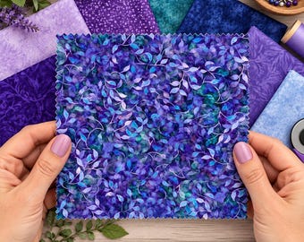 May include: A square fabric swatch featuring a dense pattern of purple and teal leaves with white outlines, held above a wooden ruler measuring 7 inches in length, surrounded by various other purple and blue fabric squares.