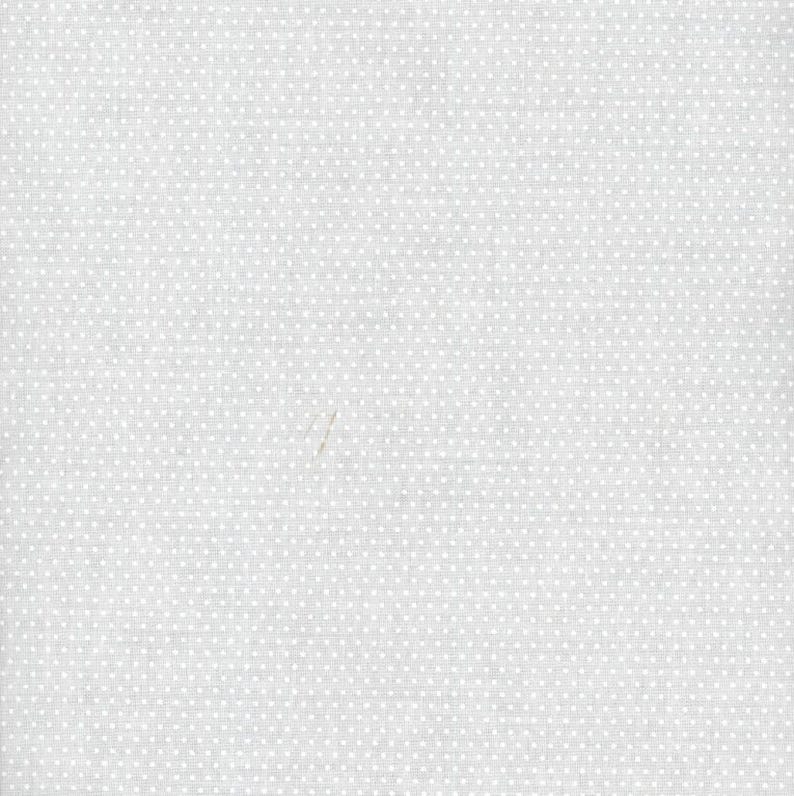 May include: A light gray fabric featuring a repeating pattern of tiny white polka dots arranged in a uniform grid. The textile surface displays a subtle woven texture with a consistent matte finish across the entire visible area of the material.