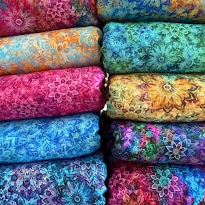 May include: A collection of folded fabric bolts stacked in two columns, each featuring a vibrant, repeating mandala pattern in various color combinations including pink, orange, blue, green, and purple with intricate floral-like geometric details.