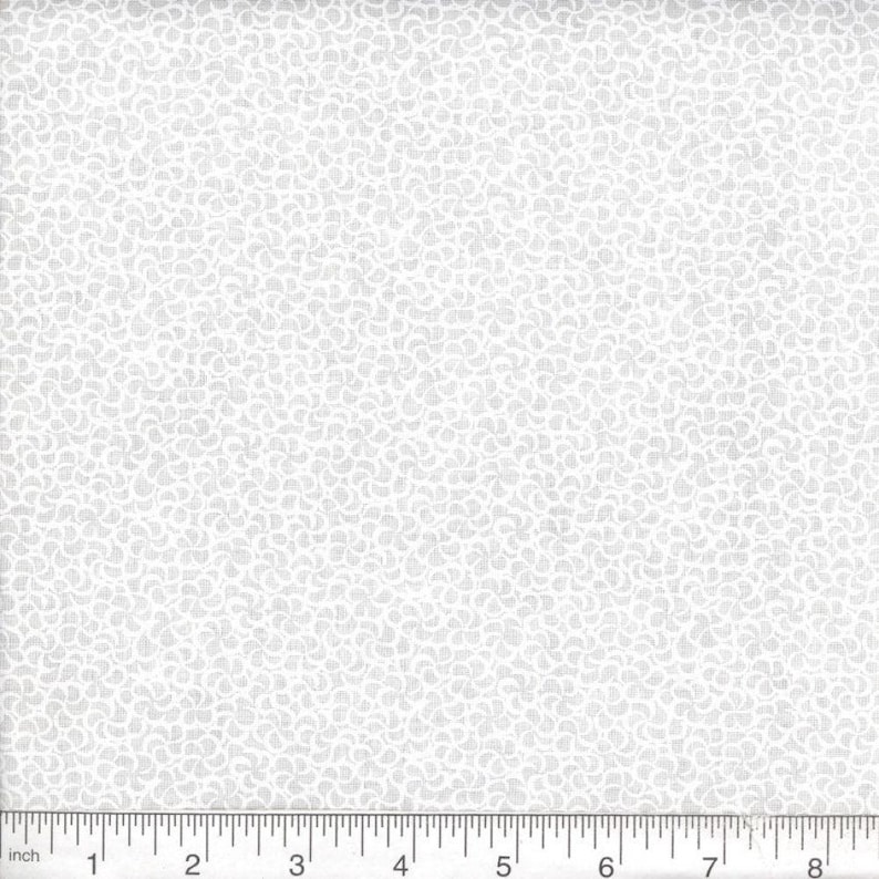 May include: A white fabric featuring a repeating pattern of small, light gray curved shapes. A ruler is positioned along the bottom edge, showing a scale in inches that spans from zero to eight inches, providing a clear sense of the scale of the print.