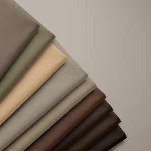 May include: A stack of folded fabric swatches arranged in a diagonal fan pattern. The collection features a neutral color palette including shades of beige, tan, taupe, olive green, chocolate brown, and dark espresso, all with a smooth texture.