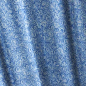 May include: A fabric textile featuring a repeating pattern of swirling, circular motifs in shades of light and medium blue against a white background. The material displays soft folds and drapes, creating a textured appearance across the surface.