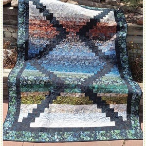 May include: A colorful quilt with a mirrored design, featuring a patchwork of blues, greens, browns, and whites. The quilt is bordered with a floral pattern and includes the text "Mirrored A 2 1/2" Strip Quilt" and "Quilting Renditions".