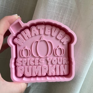 May include: Pink silicone mold for making a pumpkin-shaped cake or cookie. The mold features the text "Whatever Spices Your Pumpkin".
