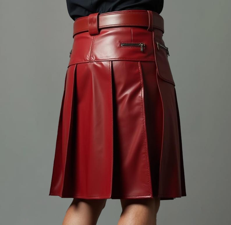 Op de afbeelding: Een rode leren kilt met bijpassende riem. De kilt heeft plooien, een zak met ritssluiting en een getailleerde pasvorm. De riem heeft een gespsluiting. Het kledingstuk is gemaakt van glanzend, glad leer.