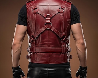 May include: A burgundy leather vest with a harness design. The vest features multiple straps, metal rings, and buckles. The person is wearing a black shirt and leather gloves.