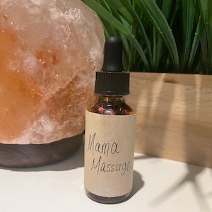 以下が含まれることがあります： 小さなガラス瓶に、ドロッパーが付いた蓋が付いており、透明な液体と乾燥した花びらが詰まっています。瓶には、"Mama Massage"と書かれた茶色の紙のラベルが付いています。