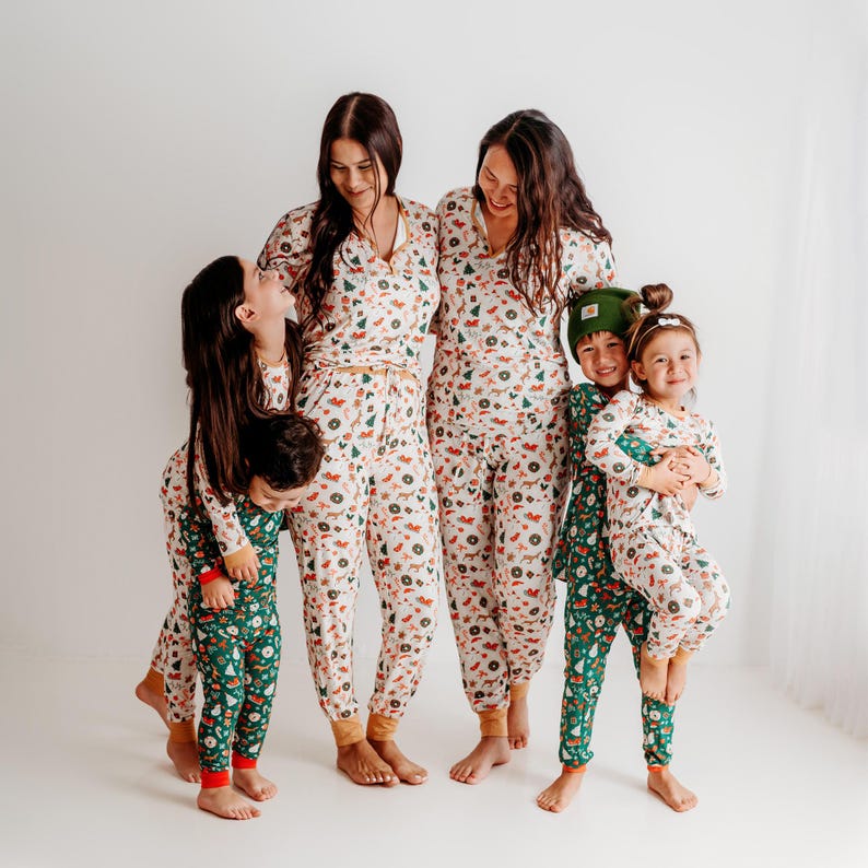May include: A family of four wearing matching pajamas with a festive holiday print. The pajamas are white with green, red, and brown accents. The print features trees, ornaments, and other holiday symbols. The family is smiling and looking at each other.